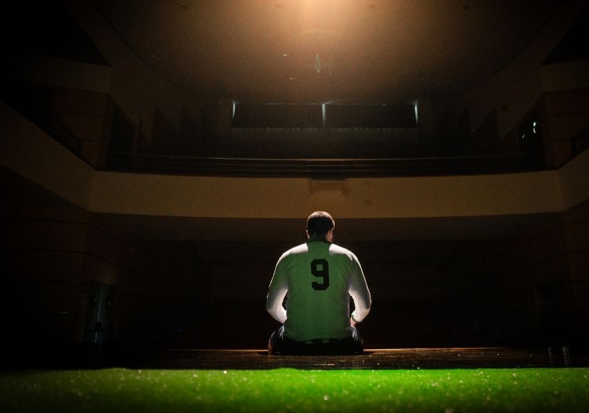 Imagen del evento:Un jugador de futbol de espaldas sentado sobre la hierva de un campo de futbol